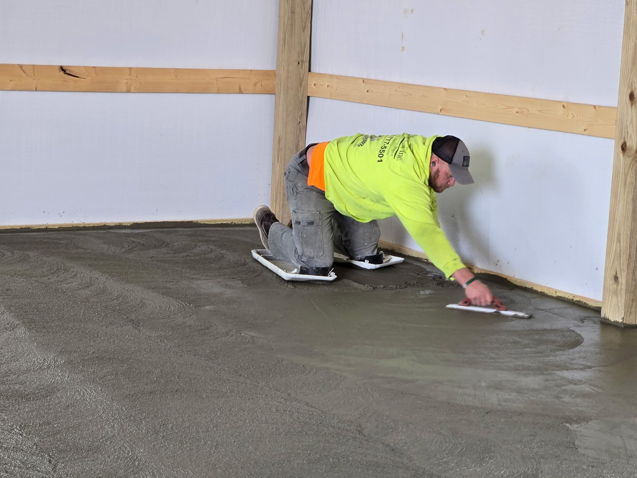 Worker finishing a concrete floor inside a newly framed pole barn